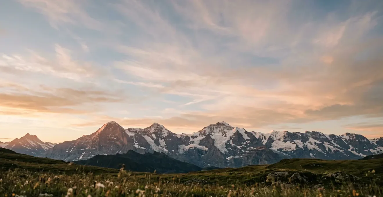 Weites Alpenpanorama mit schneebedeckten Gipfeln und dramatischem Himmel bei Sonnenaufgang, Symbol für Ruhe und Perspektive
