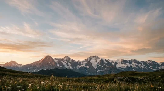 Weites Alpenpanorama mit schneebedeckten Gipfeln und dramatischem Himmel bei Sonnenaufgang, Symbol für Ruhe und Perspektive