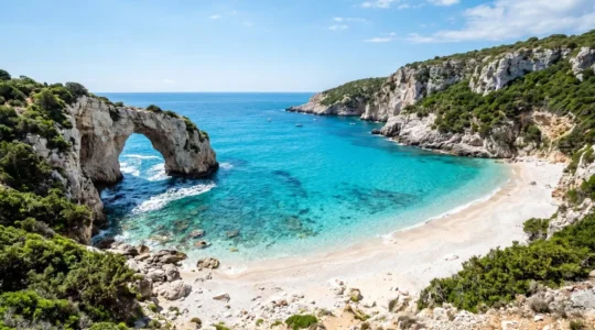 Kristallklare türkisfarbene Bucht mit weißem Strand und markanter Felsformation an der sardischen Küste